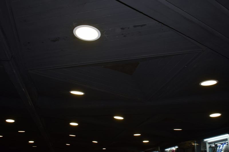 An electrician fitting a slim LED retrofit light into a ceiling to install recessed lighting