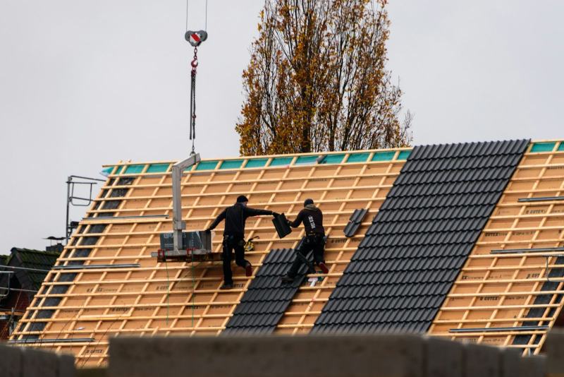 A roofer nailing a new plywood sheet to the rafters to replace roof decking before new shingles