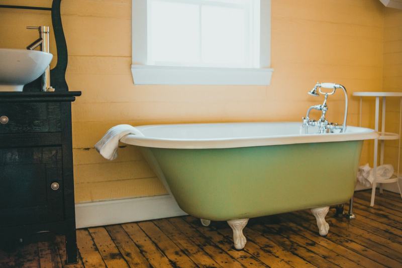 A technician spraying a glossy white coat to reglaze a bathtub after sanding the old surface